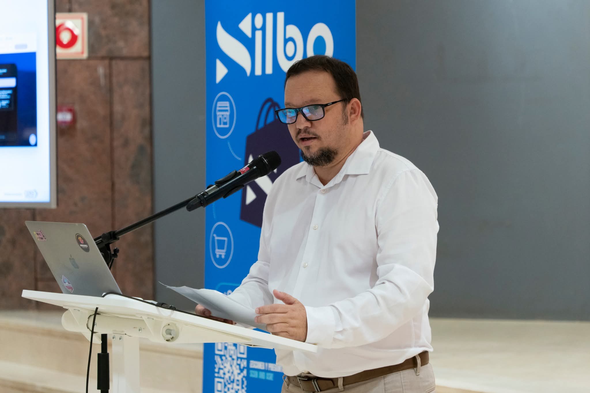 Ponente interviniendo al atril junto al roll-up de Silbo